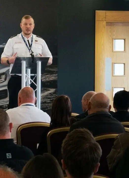 Gavin Thomas, in fire service uniform, speaking at a podium to a conference audience